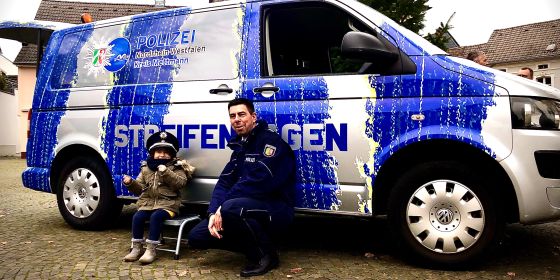Bild zeigt den neuen Streifenwagen, einen Polizeibeamten und ein Kind